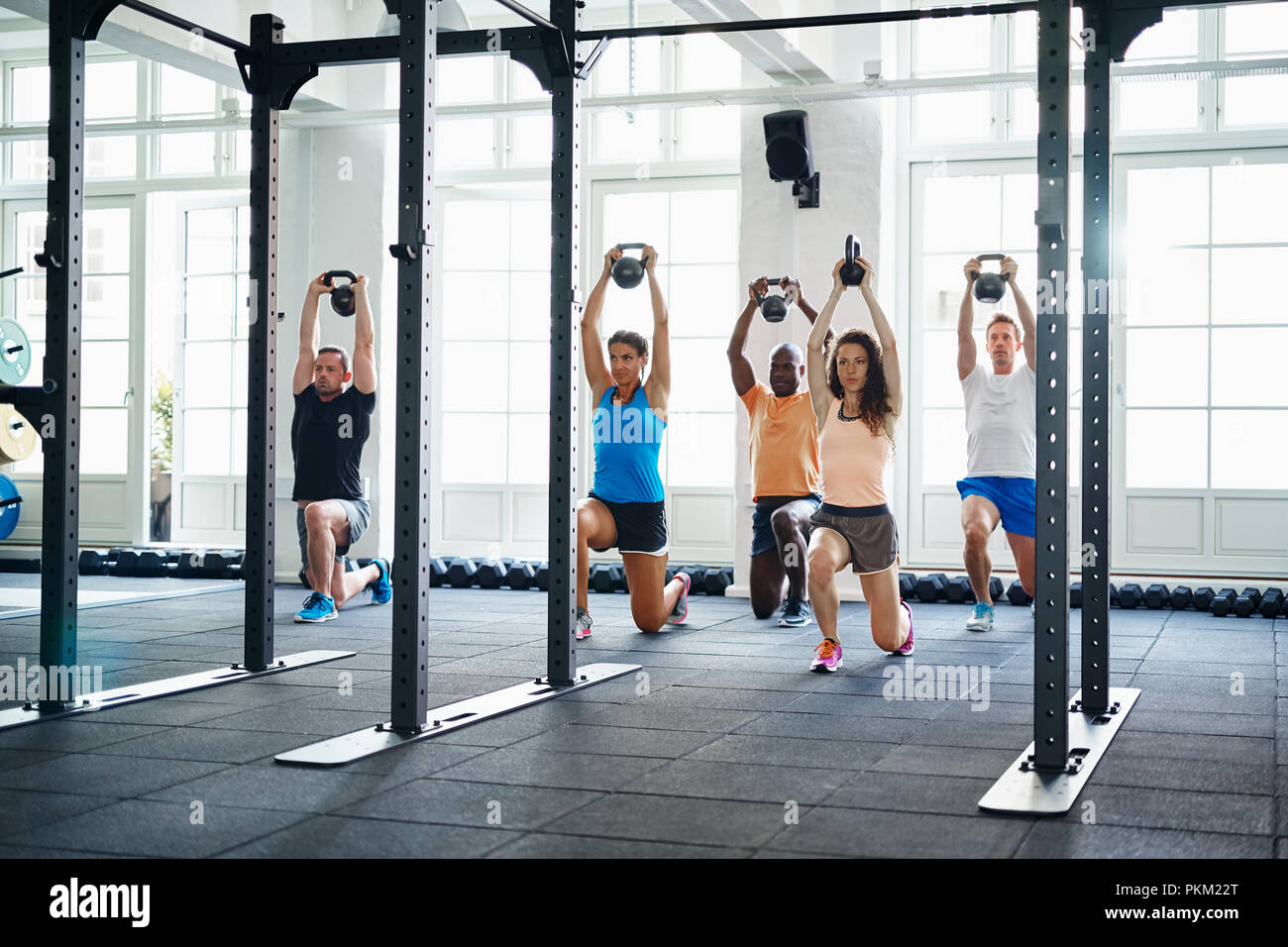 Diverse group of young people doing lunges with weights in a gym together during a workout Stock Photo