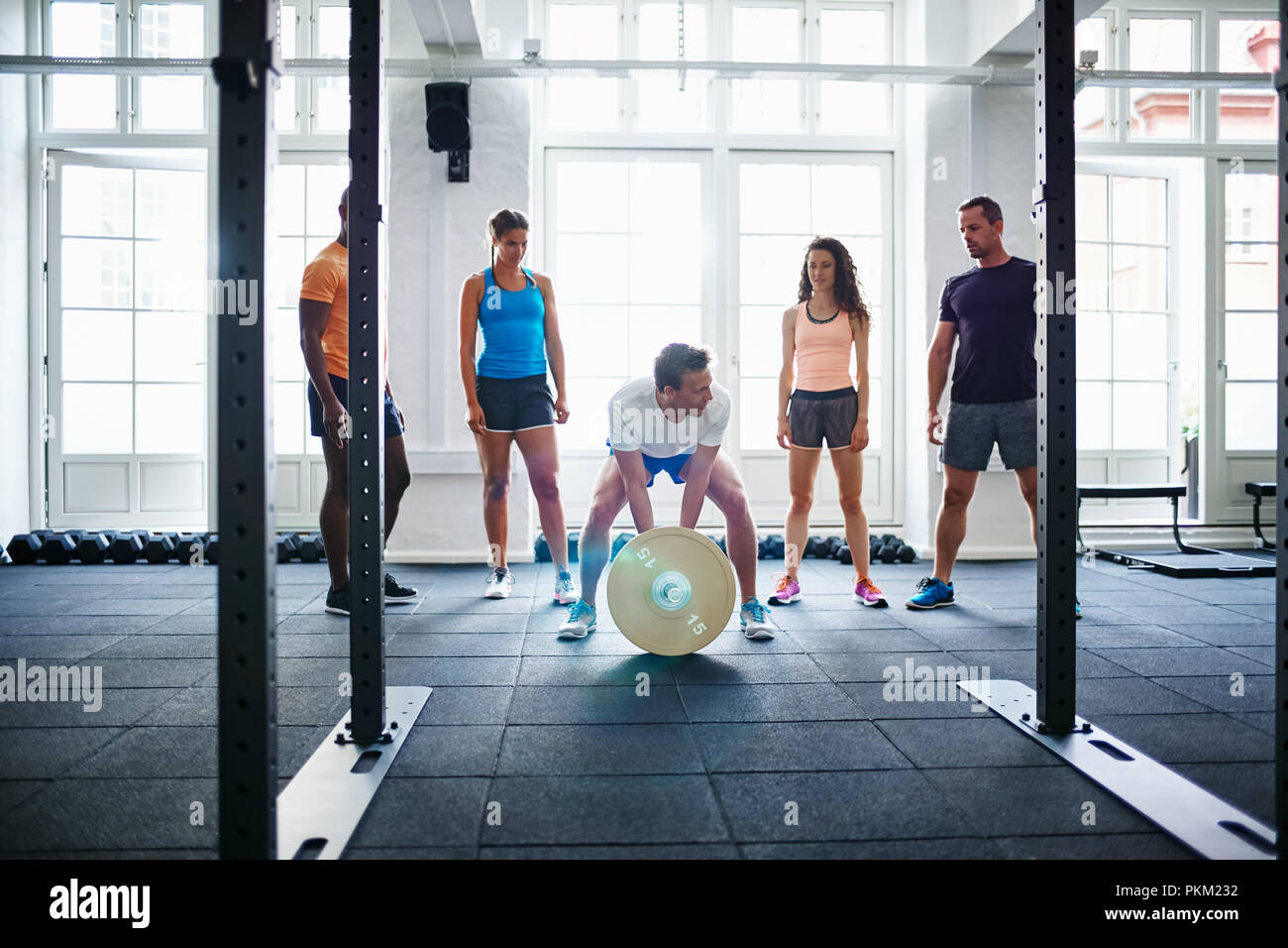Fit young man preparing to lift a barbell with a group of friends encouraging him while working out together in a health club Stock Photo