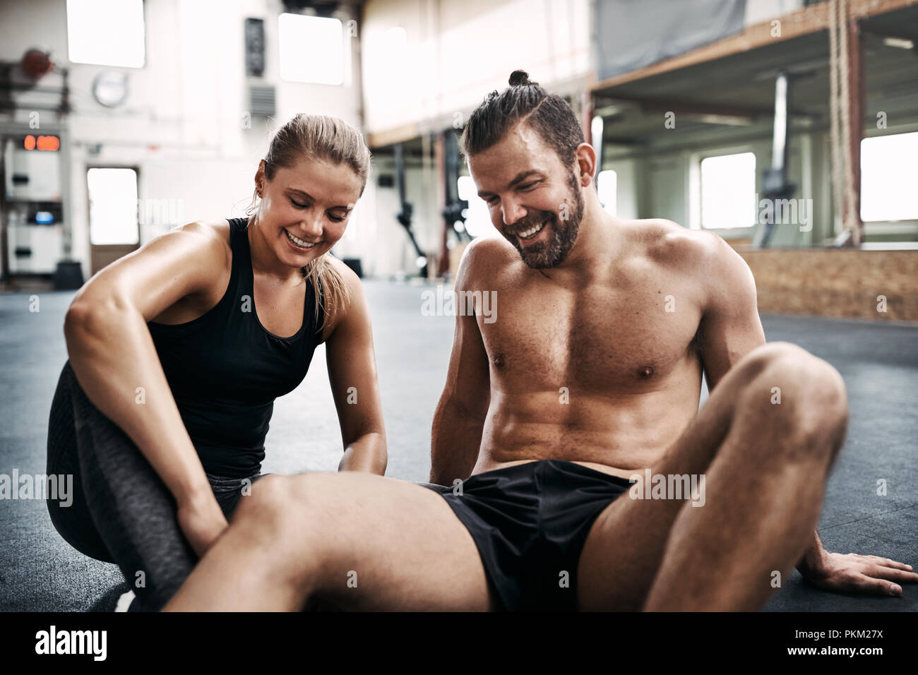 Fit young couple in sportswear sitting on the floor of a gym talking together after a workout session Stock Photo
