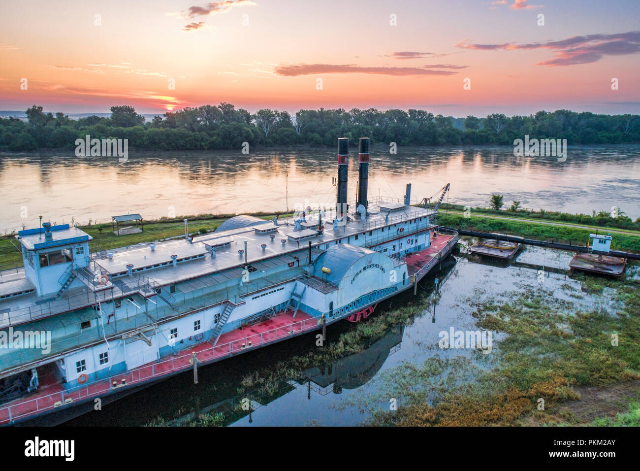 Brownville, NE, USA - July 30, 2018:  Hazy siunrise over MIssouri River with the historic dredge, Captain Meriwether Lewis, in a dry dock on a shore. Stock Photo