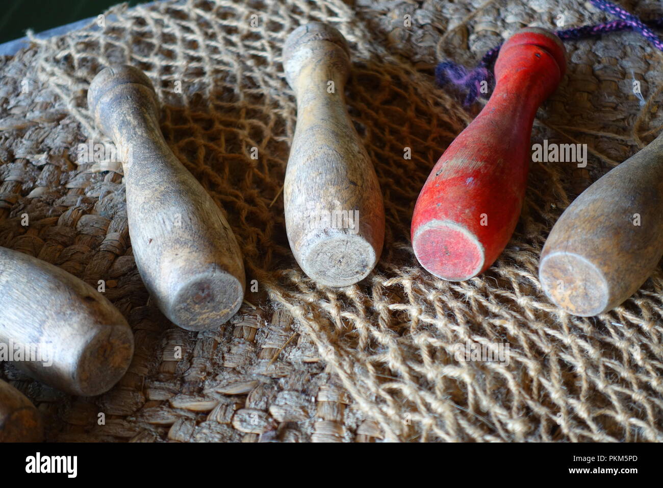 Old wooden skittles, played in medieval times, on a rough hessian backdrop. One of them is red. Stock Photo