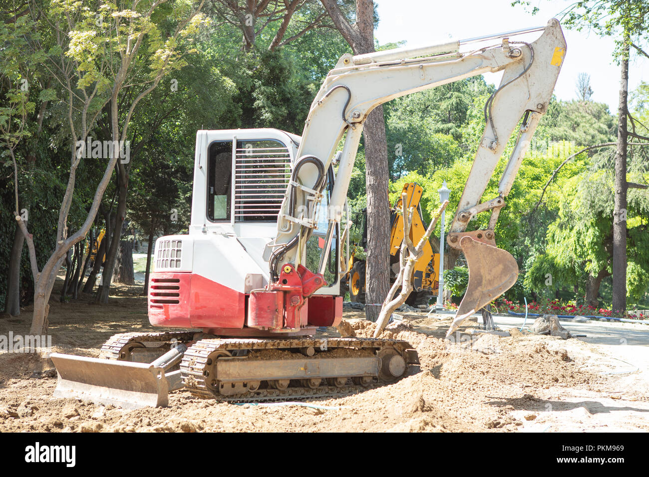 Excavator, backhoe working on soil for clear the area beside trees for new park building Stock