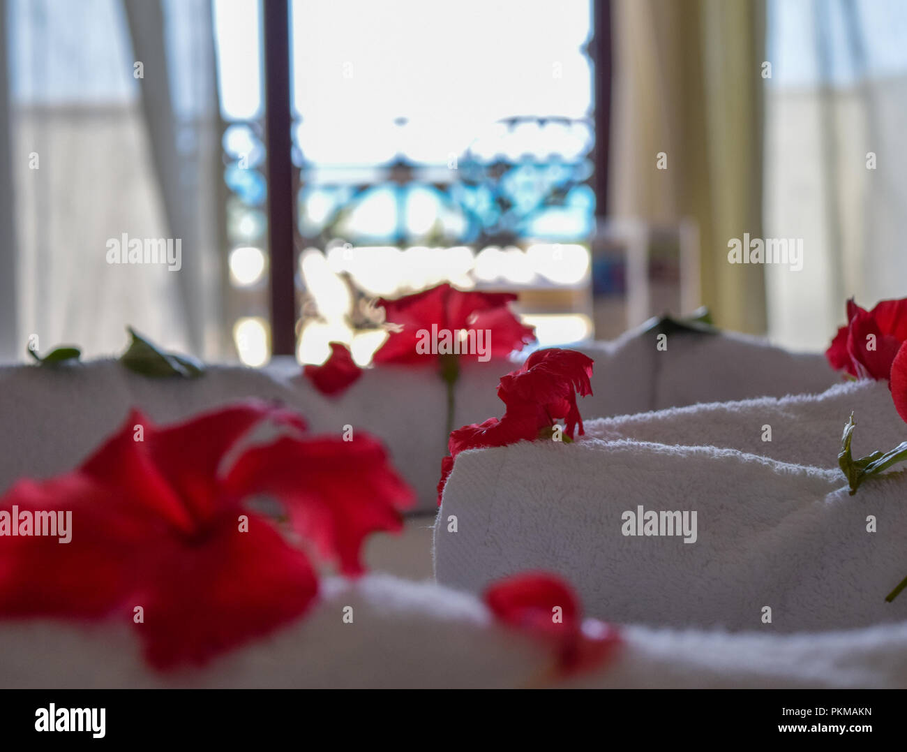 hibiscus petals on bed with beautiful sea view in background, White towels decoration surrounded by hibiscus petals Stock Photo