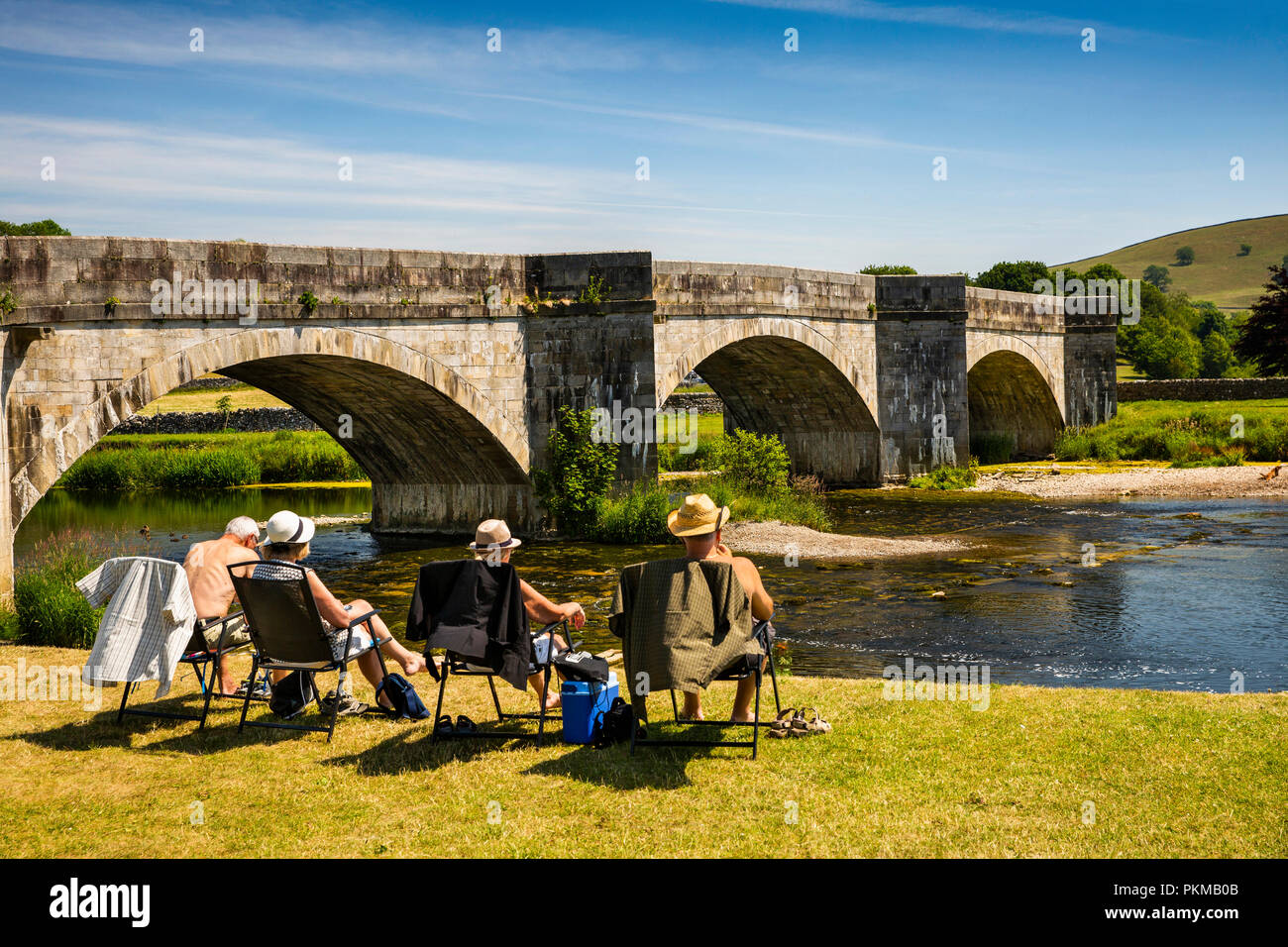UK, Yorkshire, Wharfedale, Burnsall, visitors relaxing on village green at bridge over River Wharfe Stock Photo