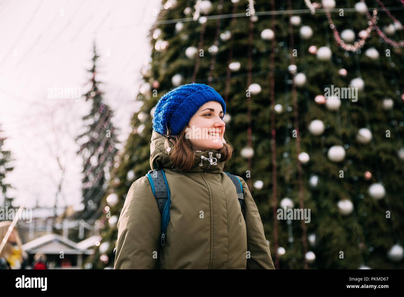 Vilnius, Lithuania. Young Beautiful Pretty Caucasian Girl Woman Dressed In Green Jacket And Blue Hat Having Fun On Background Christmas Tree. Stock Photo