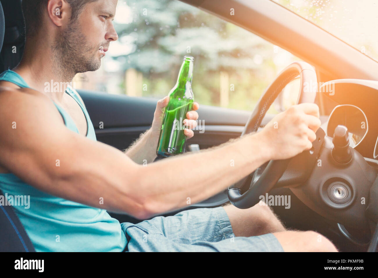 Drunk driver drinking behind the steering wheel of a car Stock Photo
