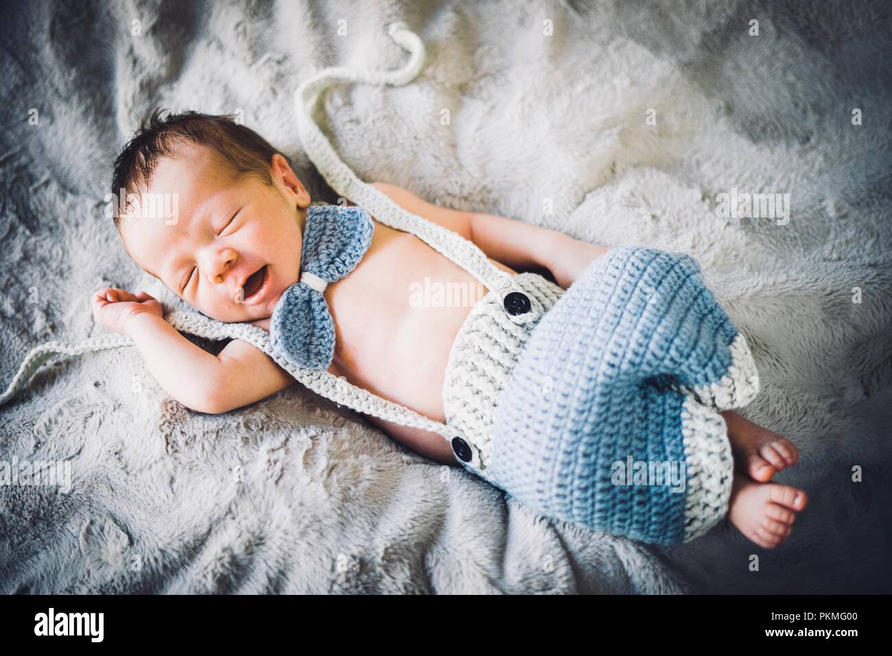 A newborn baby boy sleeping in blue and grey knitted bow tie and trousers, Portugal Stock Photo