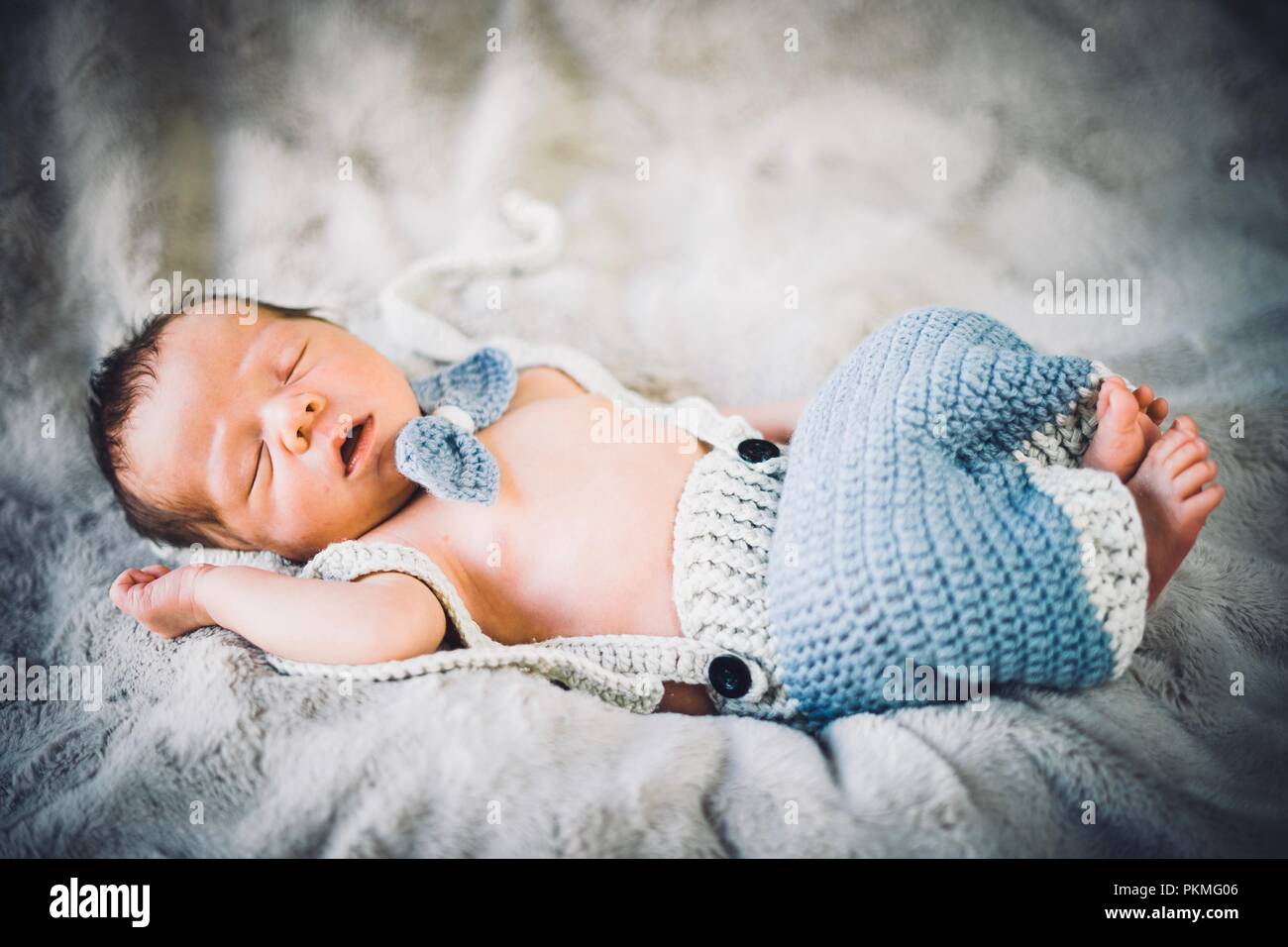 A newborn baby boy sleeping in blue and grey knitted bow tie and trousers, Portugal Stock Photo