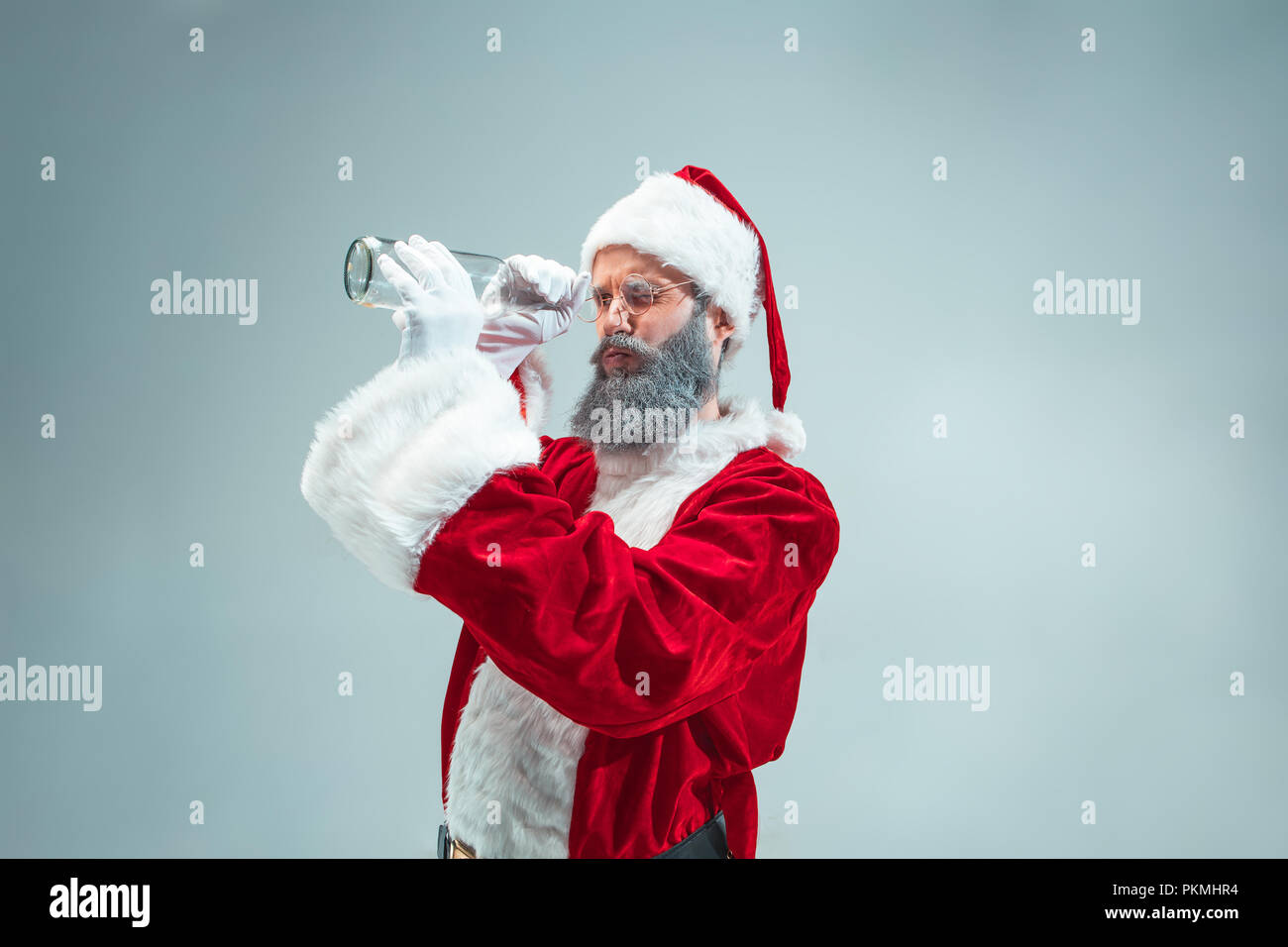 Funny guy with christmas hat posing at studio. New Year Holiday. Christmas, x-mas, winter, gifts concept. Man wearing Santa Claus costume on gray. Copy space. Winter sales. Stock Photo