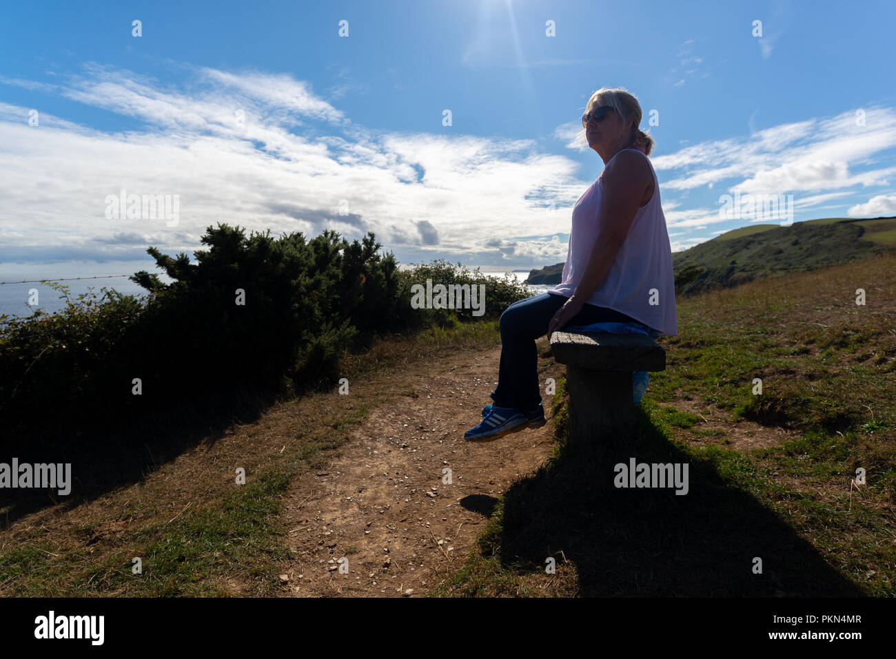 Woman sitting on a bench at the top of cliffs looking out to sea and ...