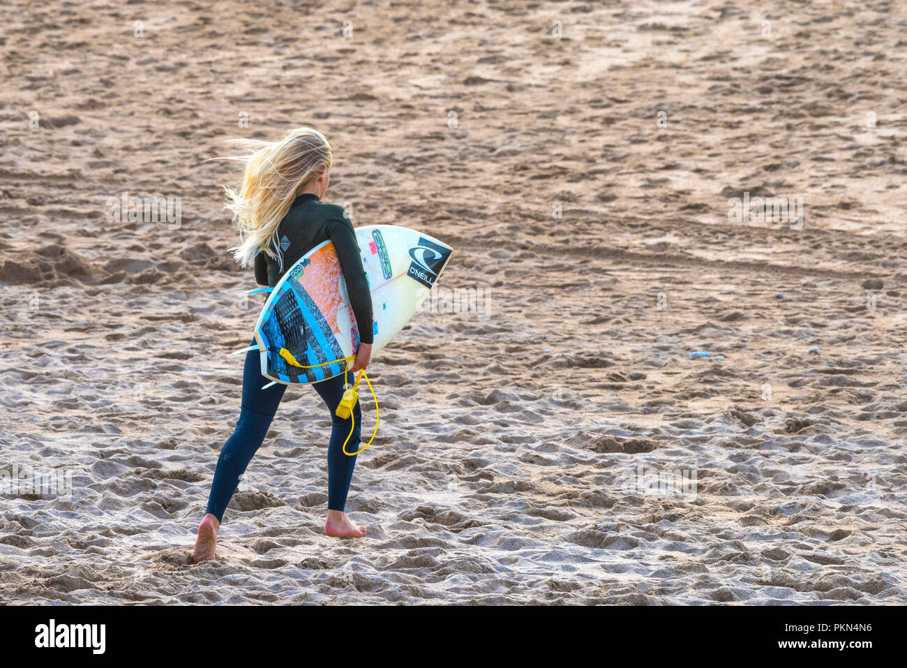 Surfing UK. A young surfer carrying her surfboard and running acros Fistral Beach in Newquay Cornwall. Stock Photo