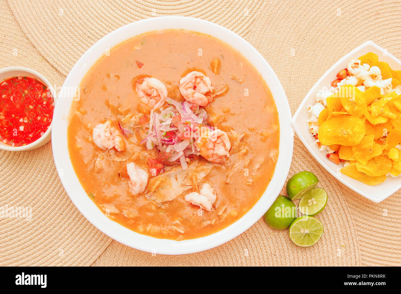 Above view of Ecuadorian food: shrimp cebiche with some chifles inside white bowl, lemon and red spicy salad inside a white bowl in a wooden table background Stock Photo