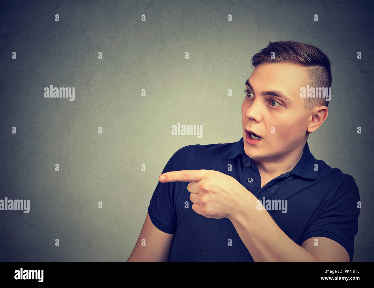 Young astonished man pointing away in disbelief standing on gray background Stock Photo