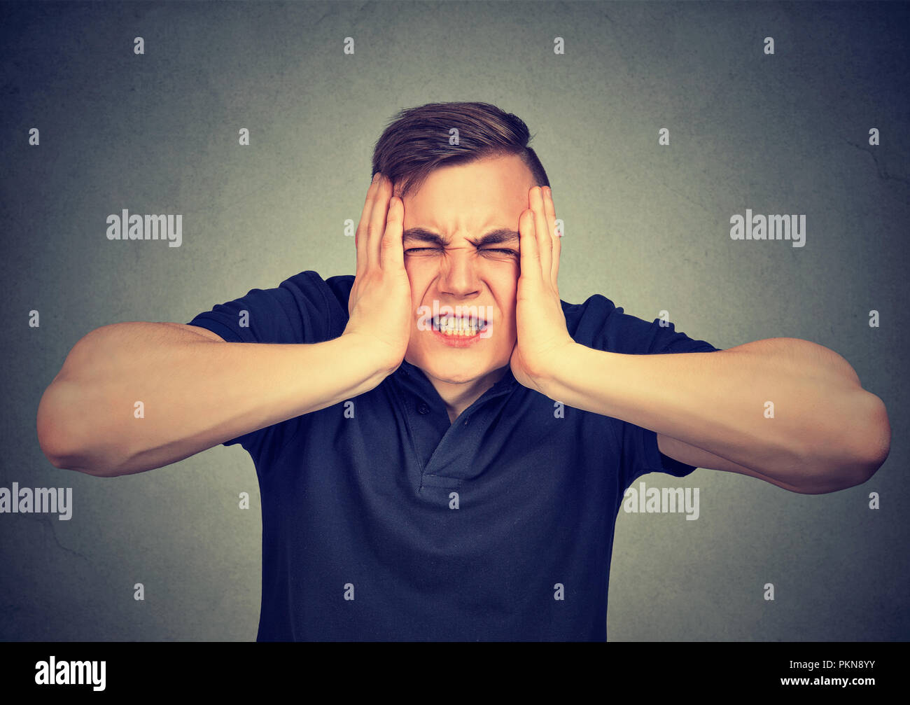 Young man suffering from pain and stress and squeezing head with hands on gray background Stock Photo