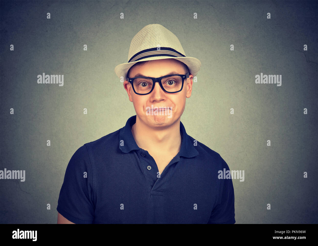 Young nerd man in eyeglasses and hat making eccentric face expression looking at camera Stock Photo