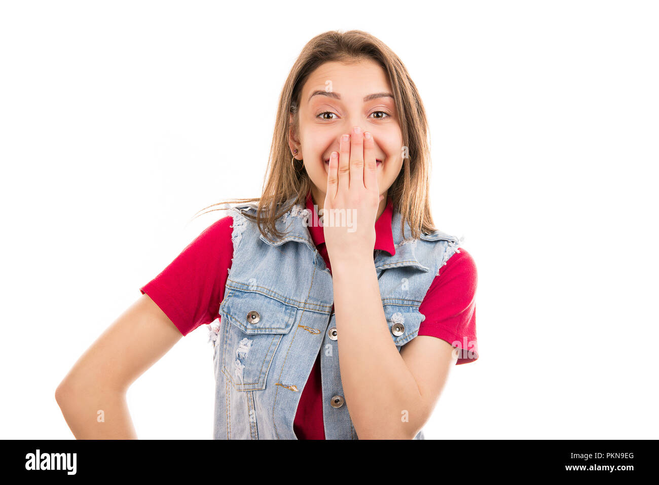 Pretty teenager woman in denim vest covering mouth in surprise isolated on white background Stock Photo