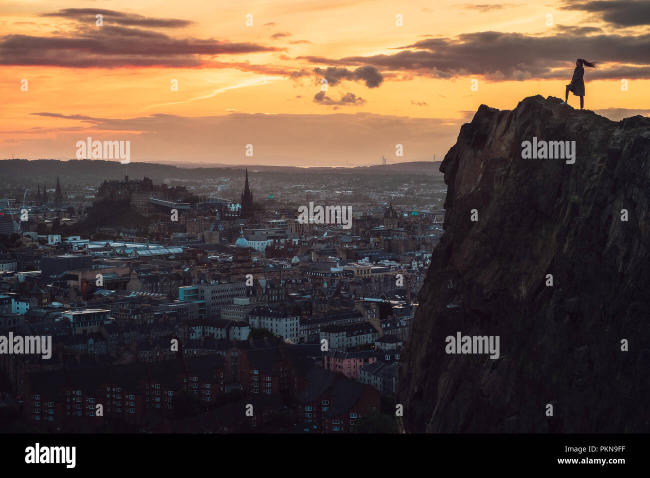 Contour of a girl standing on a rock and looking from above to a sunset city, Edinburgh, Scotland, United Kingdom Stock Photo