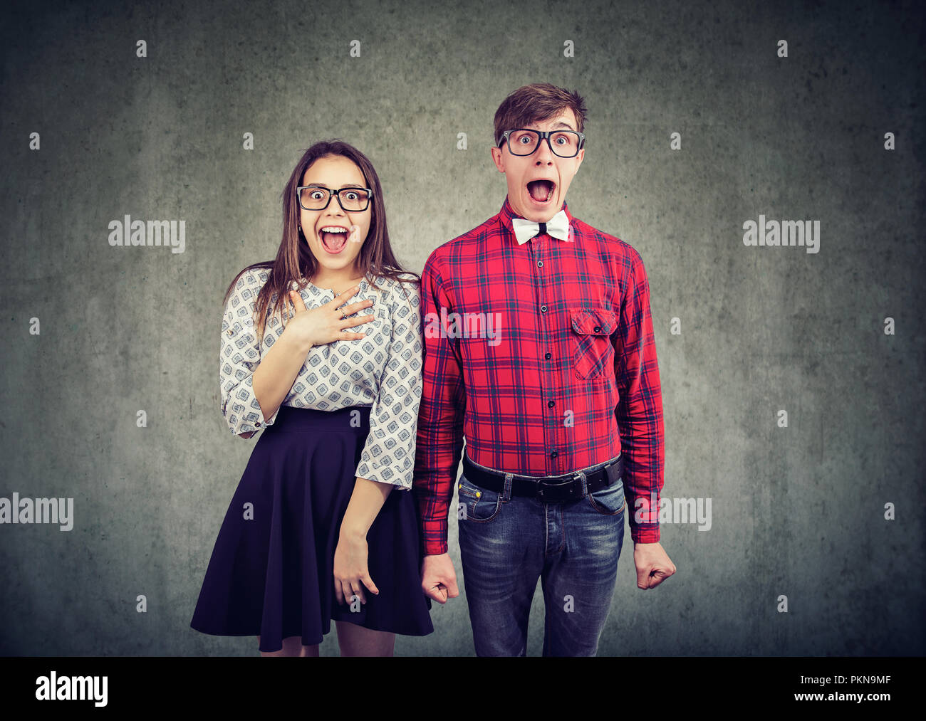Young modern man and woman in eyeglasses screaming with astonishment and looking at camera on gray background Stock Photo