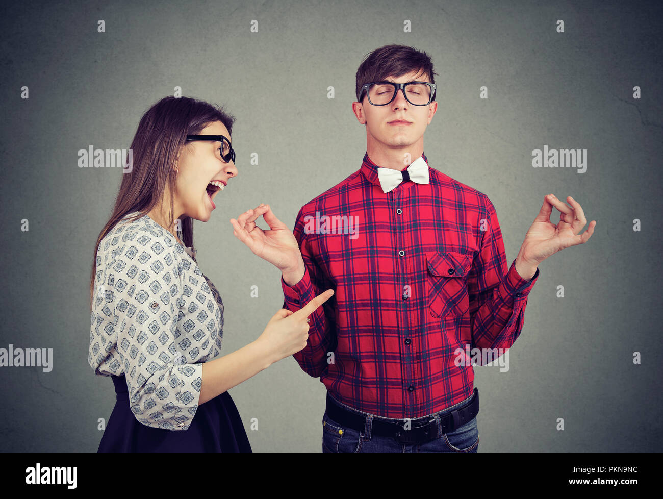 Young woman in anger yelling at boyfriend in glasses trying to keep calm in meditation Stock Photo