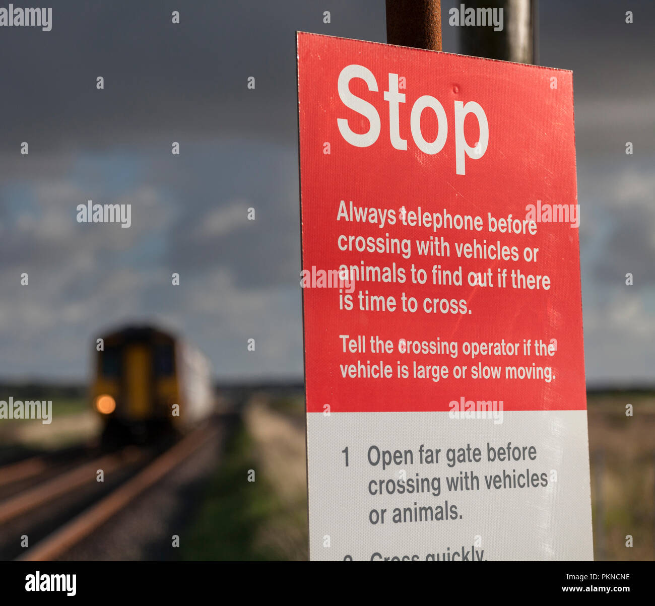 A train approaching a gated user worked level crossing showing the stop sign and user instructions on the Cumbrian coast line at Dunnerholme Stock Photo