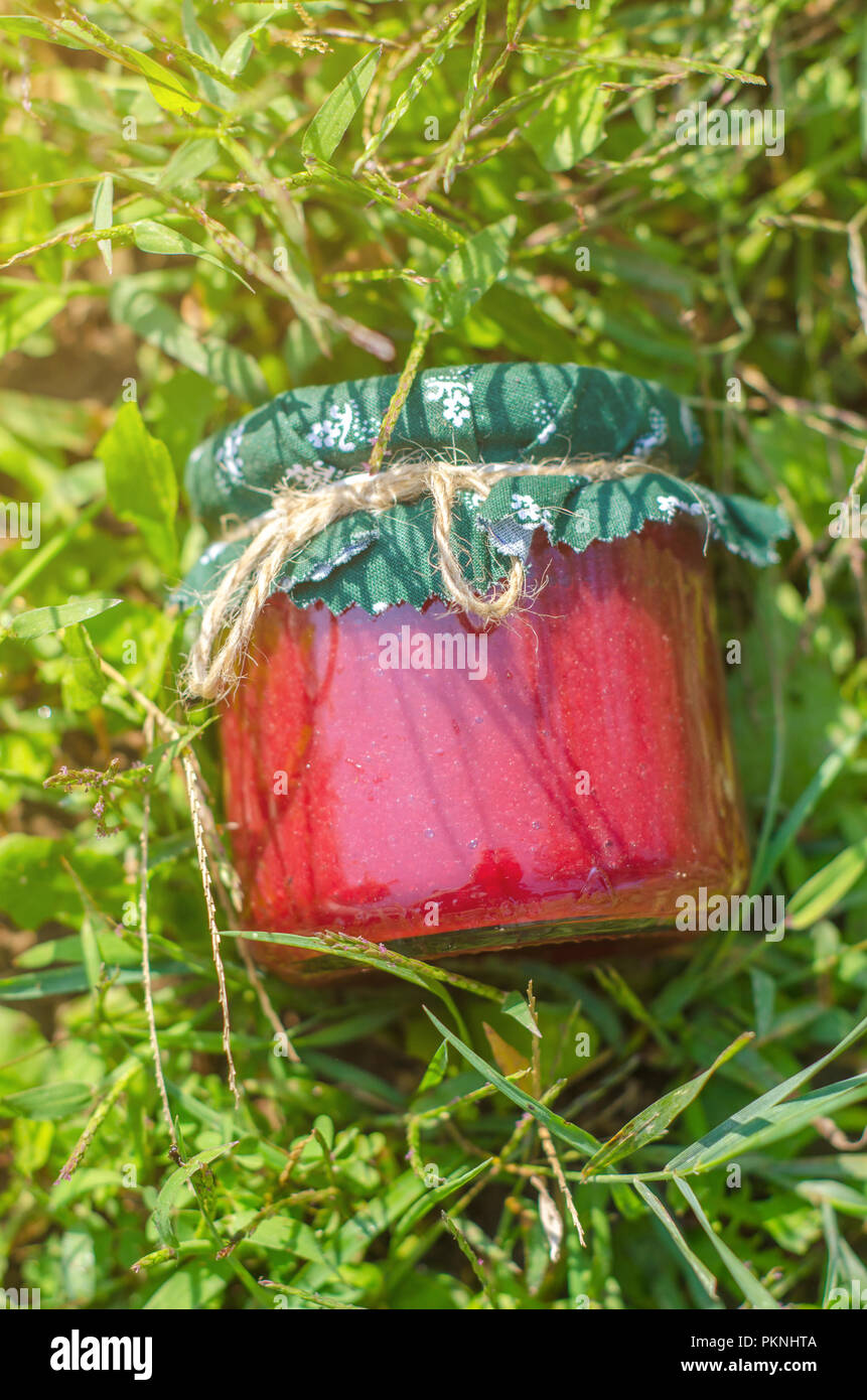 Glass jar with strawberry jam, on green natural background Stock Photo