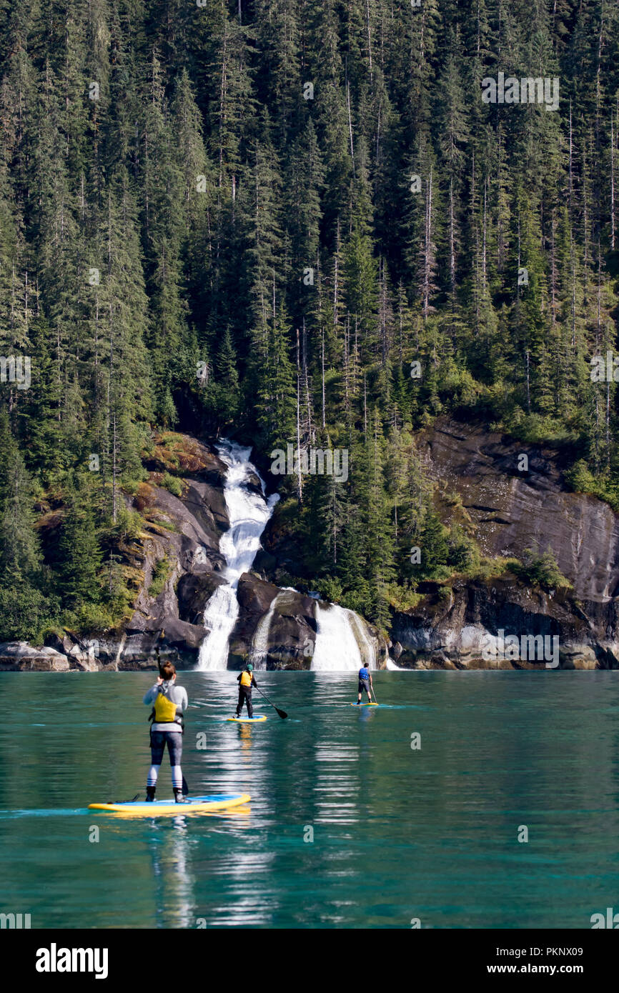 Stand up paddle boarding in front of a big waterfall in the glacially carved fjord of Tracy Arm in Southeast Alaska USA Stock Photo