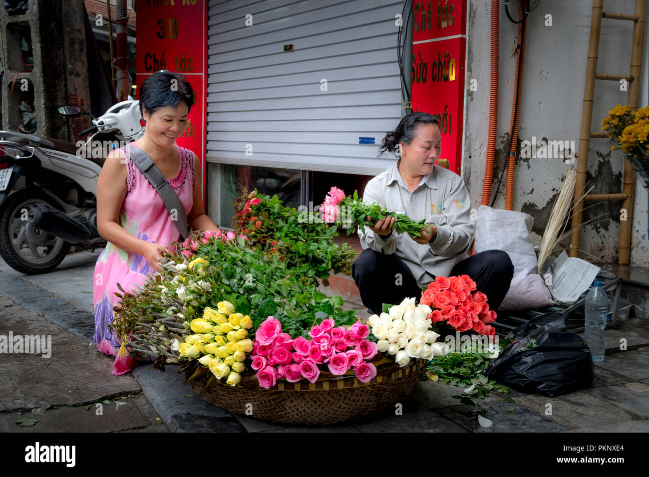 Scene two happy smiling women buying fresh flowers on an old street in Hanoi, Vietnam Stock Photo