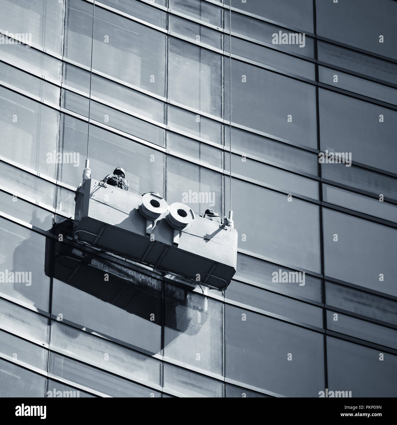Office building maintenance, glass facade cleaning with cradle. Square blue toned photo Stock Photo