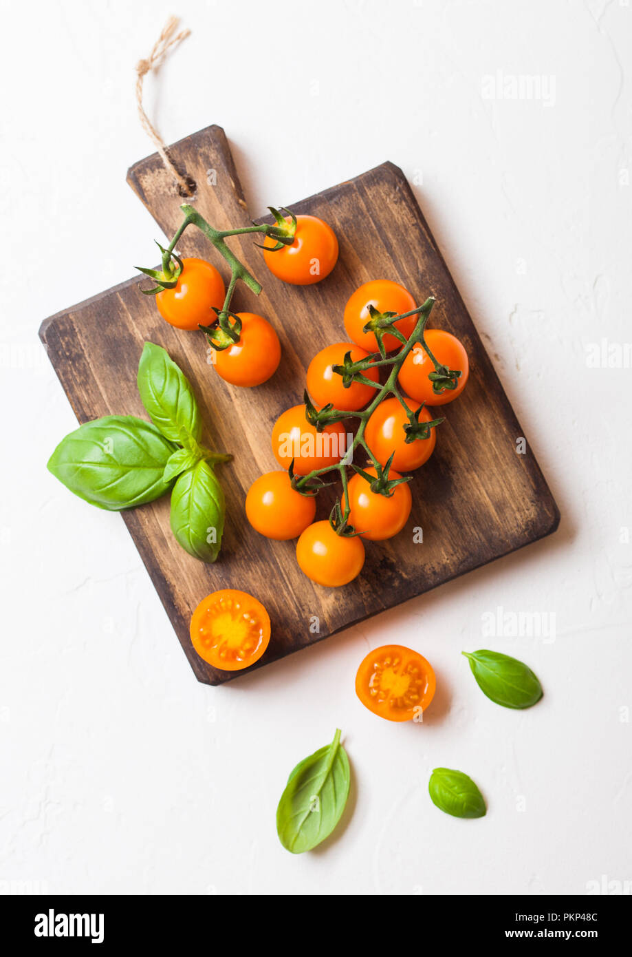 Organic Cherry Orange Rapture Tomatoes on the Vine with basil on chopping board on white background. Stock Photo
