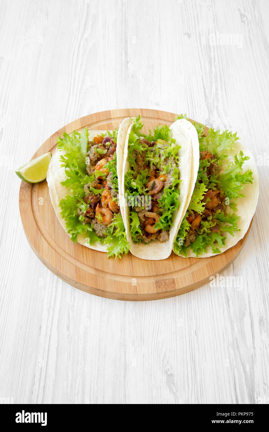 Shrimp tacos on round bamboo board on white wooden background, high angle view. Mexican cuisine. Stock Photo