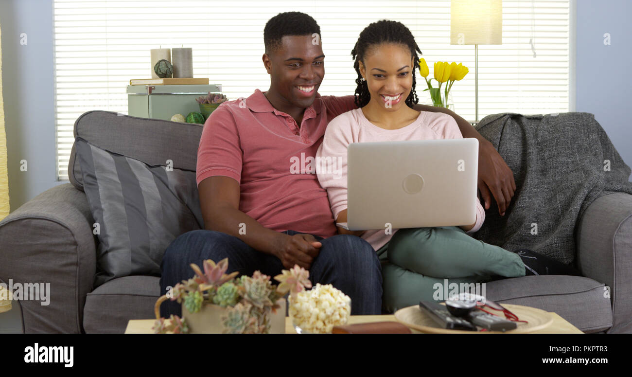 Happy black couple on couch browsing internet with laptop computer Stock Photo