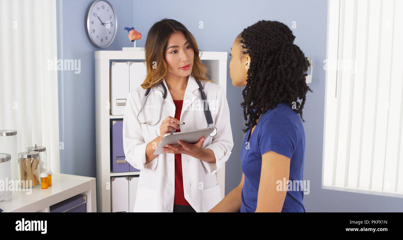 Japanese doctor taking notes and talking with African American patient