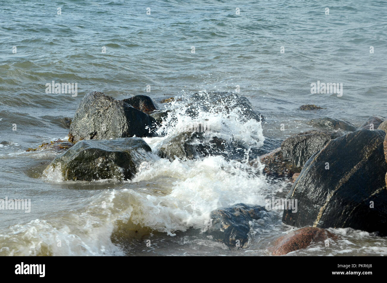 Smaller waves break on stones at a coast Stock Photo
