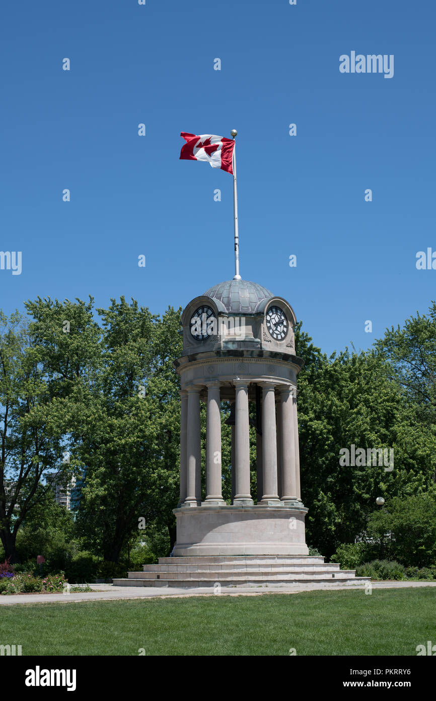 Canadian Flag Waving On The Top Of A Clock And Bell Tower In A Park With Trees In The Background Stock Photo