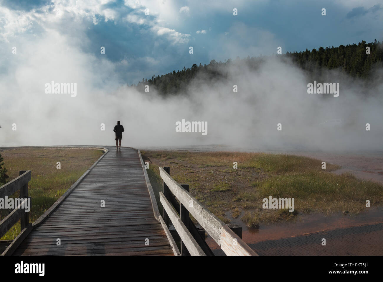 Man walking on boardwalk in Yellowstone National Park in a foggy atmosphere at Black Warrior Lake Stock Photo