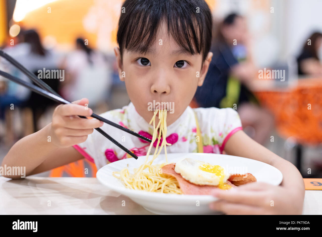 Asian Chinese little girl eating noodles with chopsticks in restaurant Stock Photo