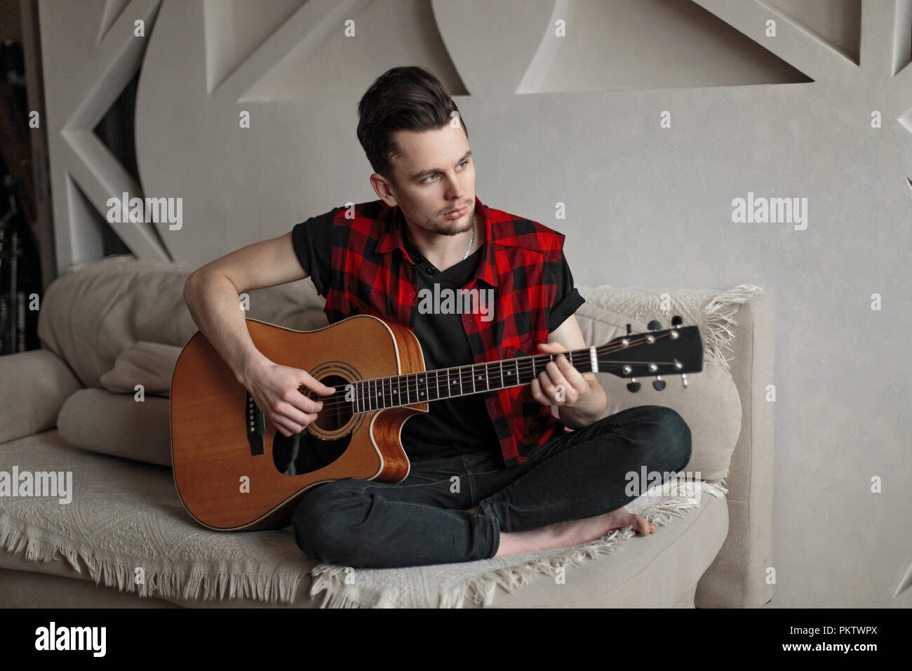 Young handsome man sitting on sofa and playing guitar Stock Photo