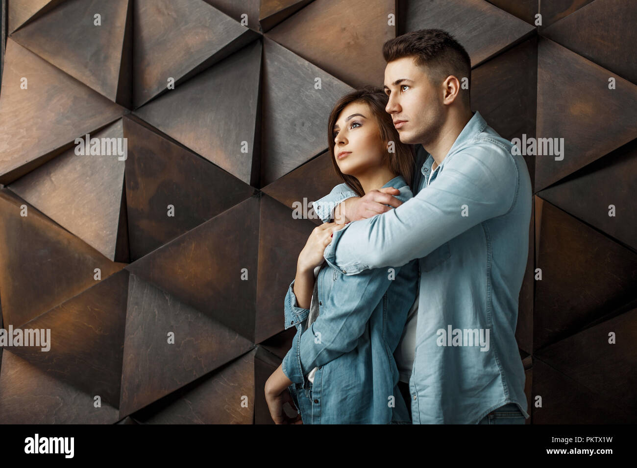 Stylish beautiful young couple in denim blue clothes near a wooden patterned wall Stock Photo