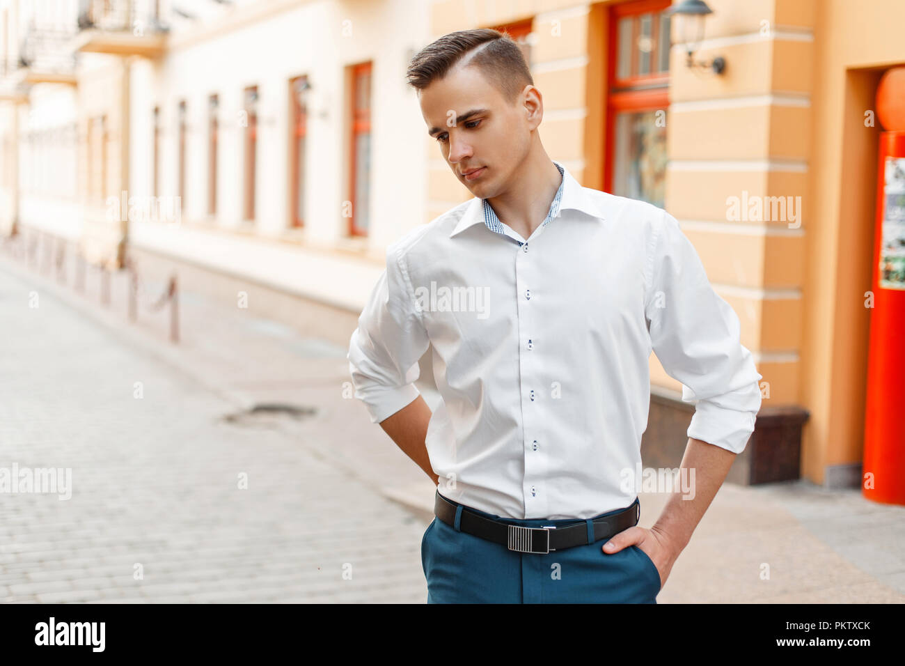 Handsome stylish man in a white elegant shirt and blue pants in the city Stock Photo