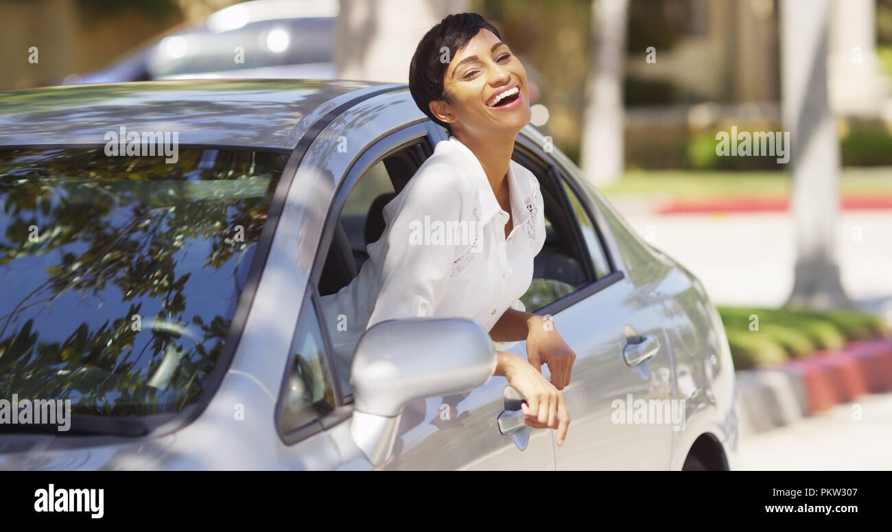 Happy black woman leaning out car window with hands in the air Stock
