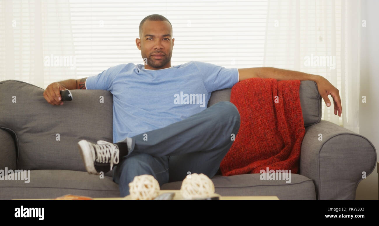 African man sitting on couch watching tv Stock Photo - Alamy