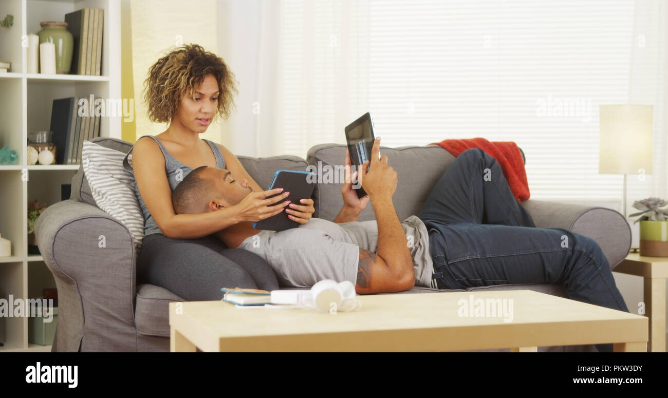 Black couple using their tablets on couch Stock Photo