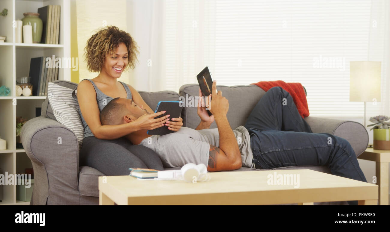 Black couple using their tablets on couch Stock Photo