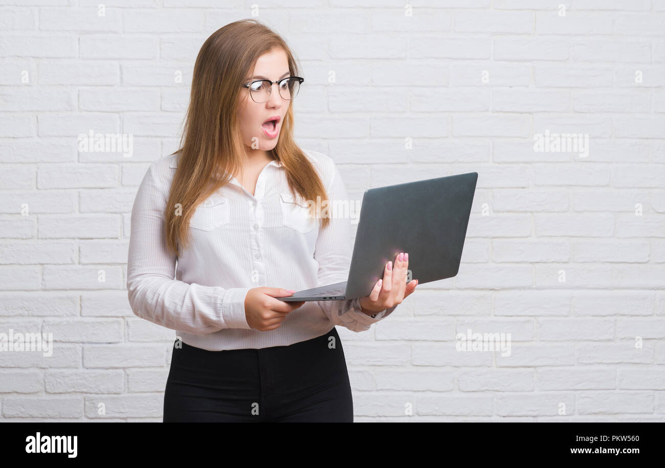 Scared Computer Young adult business woman over white brick wall holding computer ...