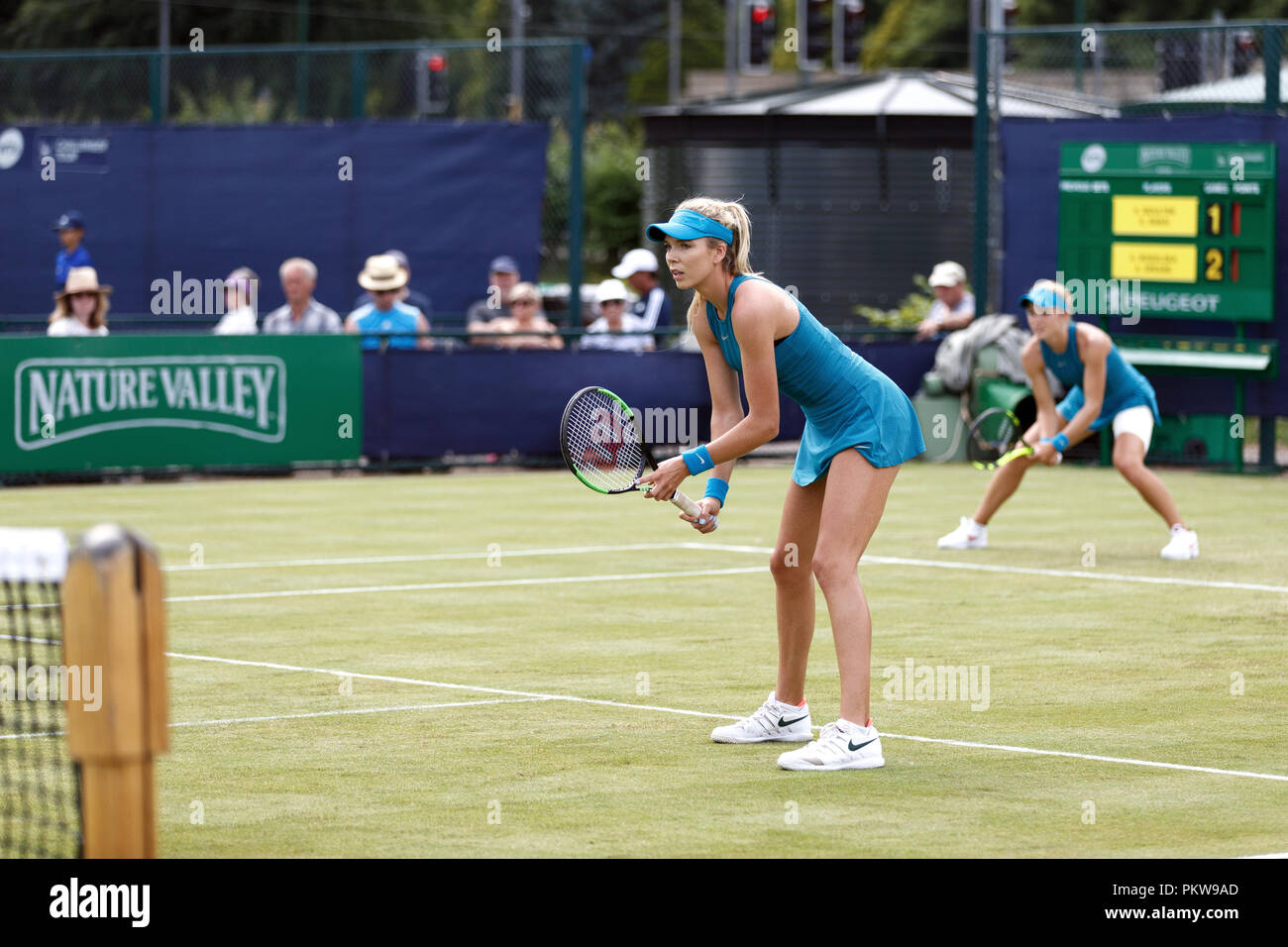 British tennis players Katie Boulter (foreground) and Katie Swan (background) await their opponent's serve during a women's doubles match at a professional grass court tournament in the United Kingdom. Boulter and Swan played together in matching outfits. Stock Photo