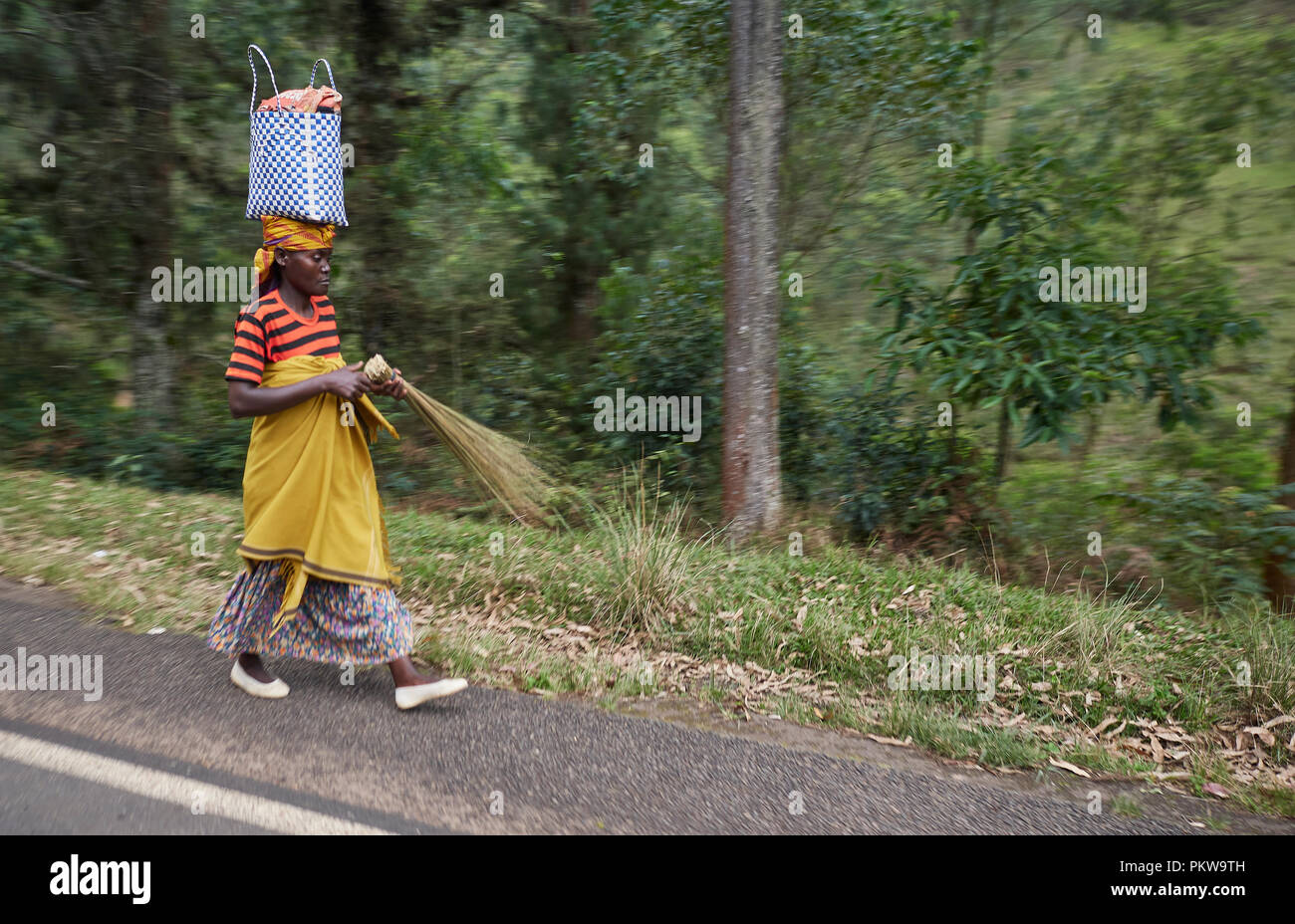 lady walking on the road with a colourful outfit and a bag on her head carring a grass brush/broom Stock Photo