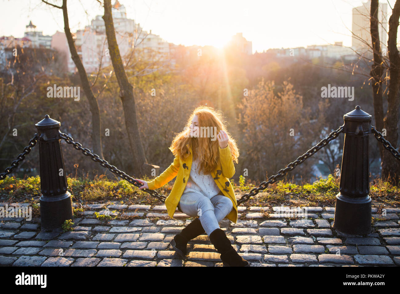 Red hair beautiful woman wearing yellow coat walking outdoors. Autumn time, city on background Stock Photo