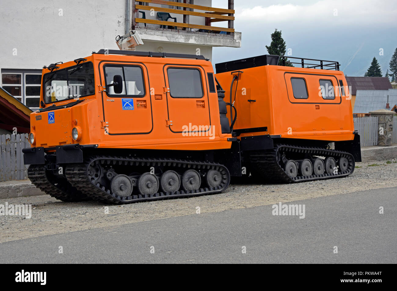 Orange, tracked snowcat rescue vehicle with wagon, parked at the side