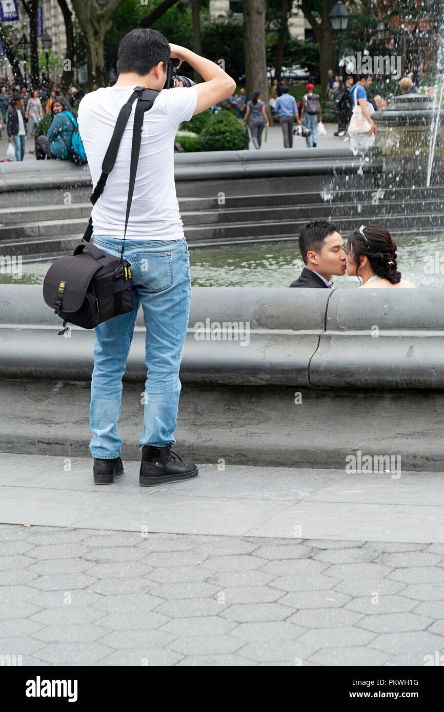 An Asian American photographer photographing an attractive Chinese couple prior to their wedding. In Washington Square Park in Greenwich Villge, NYC. Stock Photo