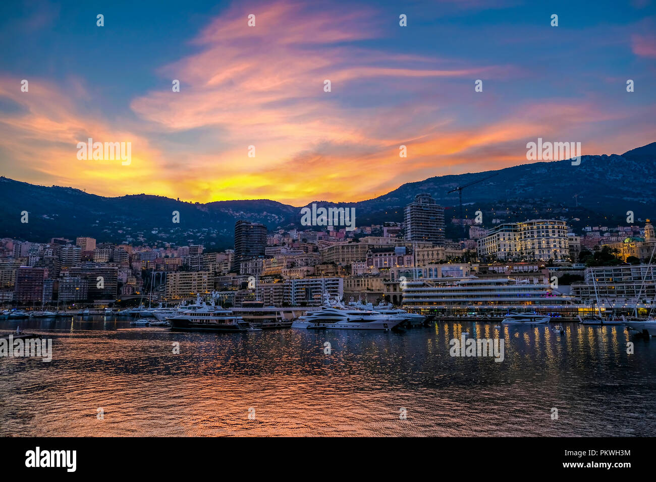 Sky appears on fire as the sun sets over the exclusive harbour at Monte Carlo Monaco and lights start to come on around the popular resort Stock Photo
